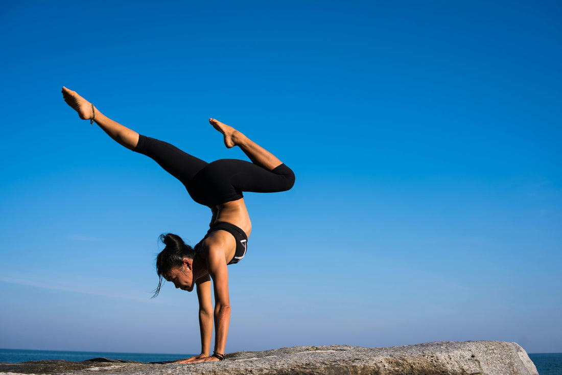 Woman performing a handstand on a rock with a blue sky in the background.