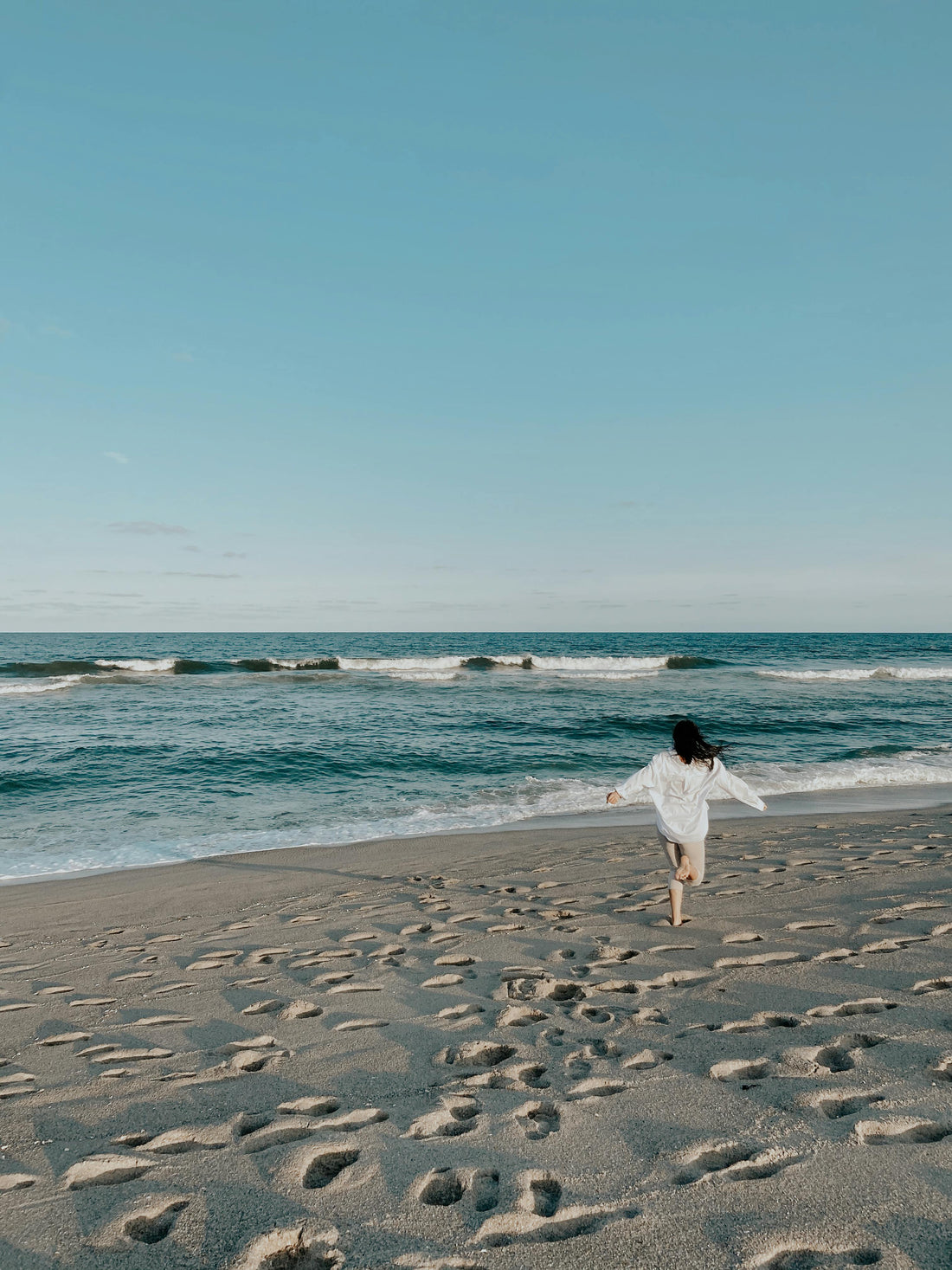 A person running on the beach with waves in the background and footprints in the sand.