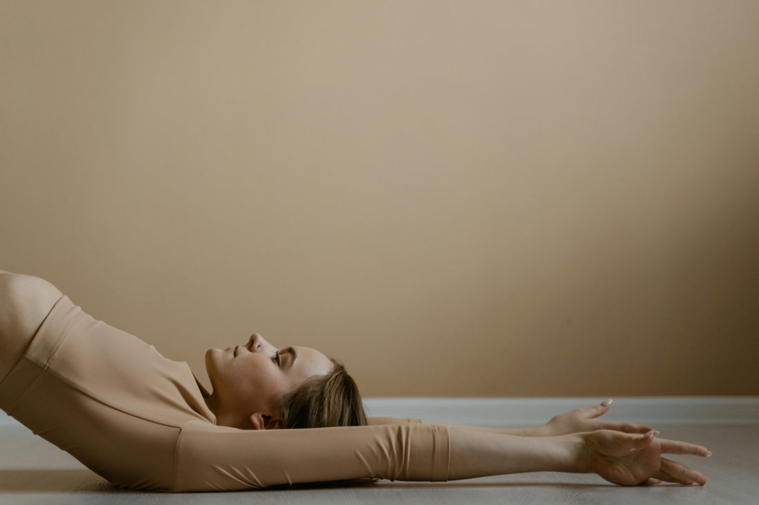 Woman practicing relaxation stretching on the floor against a warm, neutral wall in a colostrum supplement comparison article.